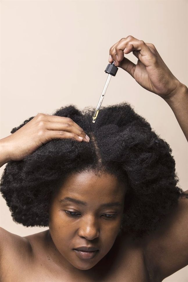 A woman applying  hair growth oil to her scalp